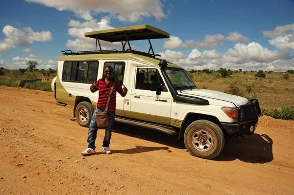 Guide with shoulder bag next to a 4x4 safari jeep on red dirt road