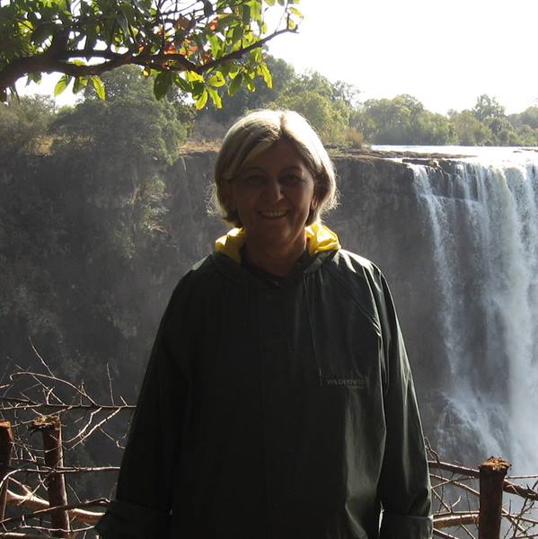 Smiling woman in green raincoat in front of Victoria Falls, water spray