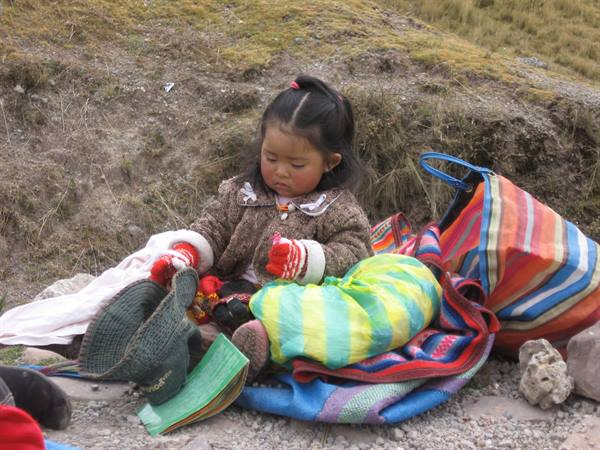 Little girl in red gloves among colorful woven bags on stony ground
