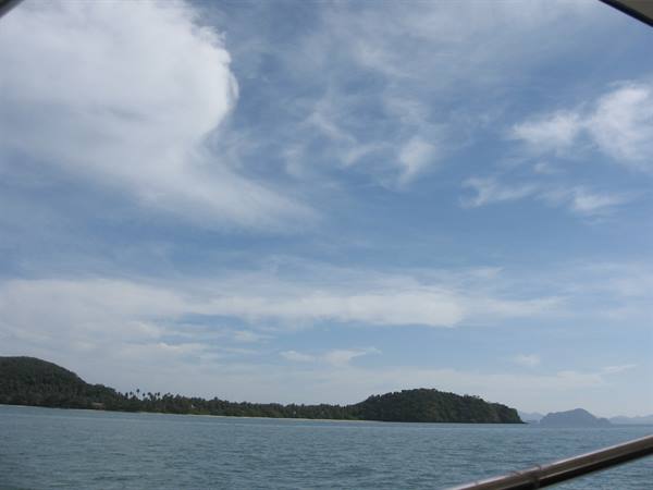 Green islands across calm sea, white clouds, sailing on a boat