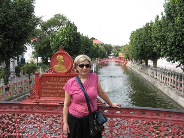 Woman in pink shirt on red cast-iron bridge over canal with fountain in Bangkok