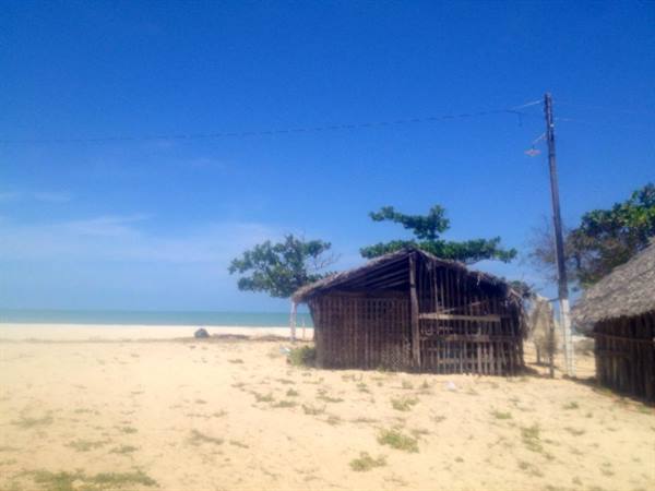 Wooden and straw hut on the sand, facing the sea under blue sky