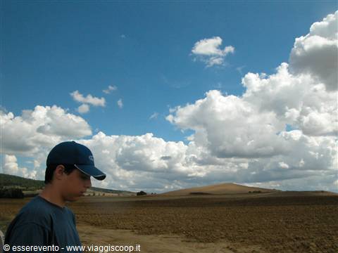 Boy in blue cap in front of plowed fields and hills under white clouds