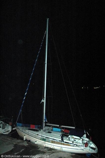 White sailboat moored at night in the harbor, mast lit in the dark