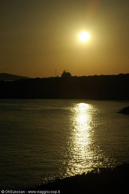 Low sun reflecting on the sea behind a small church silhouetted on the coast