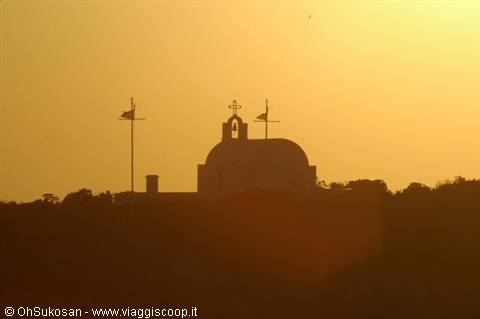 Greek church silhouetted against golden sky, bell tower and cross in backlight