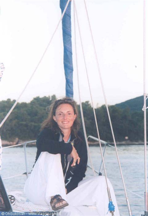 smiling woman sitting on a sailboat deck with furled mast