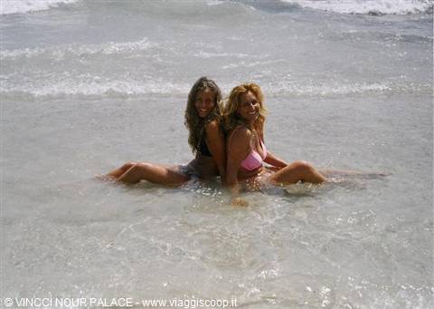 Two women in swimsuits sitting in shallow sea water at Vincci Nour Palace