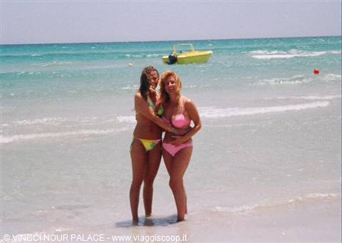 Two girls in bikinis on wet sand, yellow boat among the waves