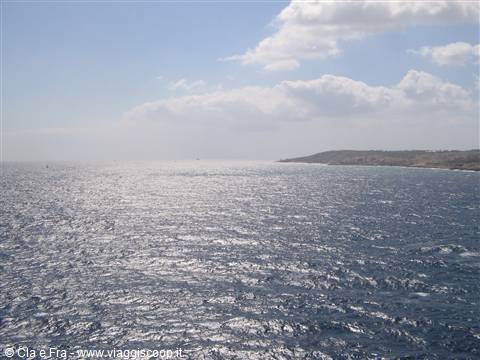 open sea with shimmering light on blue water, rocky coastline and clouds to the right