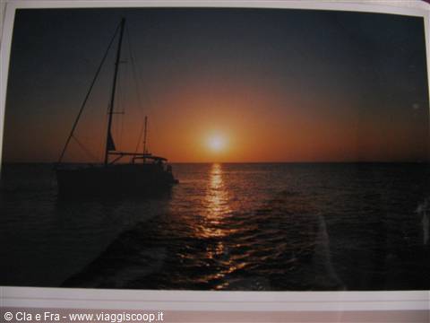 Sailboat anchored offshore at sunset, golden reflections on the sea