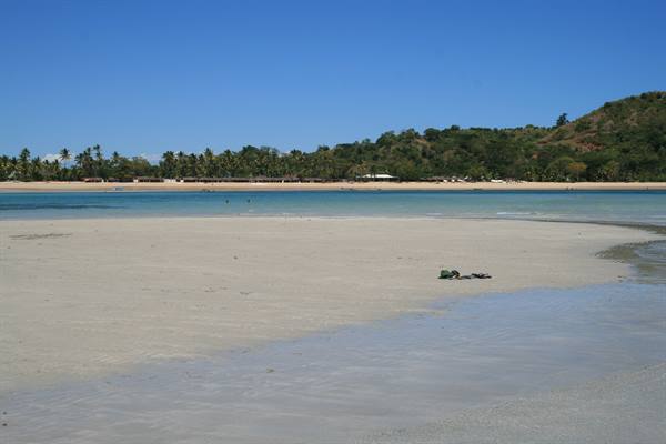 Shoes left on wet sand, tropical beach with palms and green hill