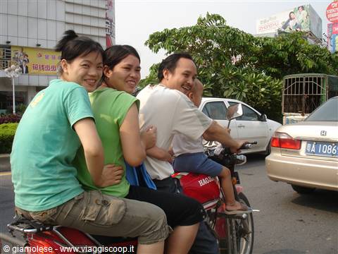 Four smiling people riding a red motorbike through busy Chinese city traffic
