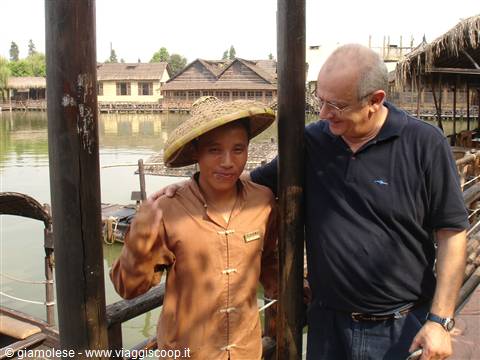 Tourist beside girl in straw hat on lakeside wooden stilt village