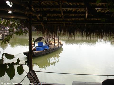 Loaded boat seen under thatched roof, green river in soft light