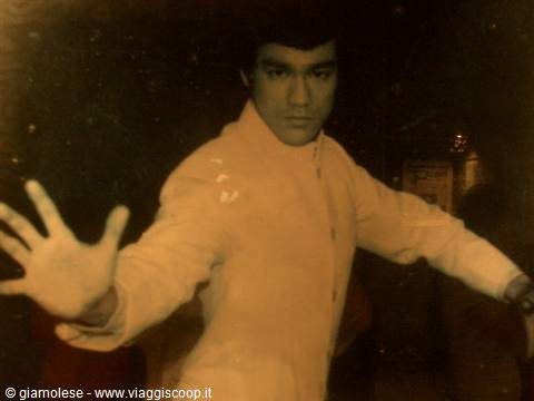 Man in white suit striking a martial arts pose, open hand toward camera