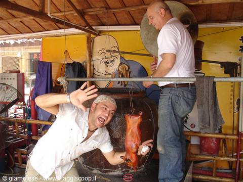 Two tourists joke around beside a roasted pig hanging on a metal pole