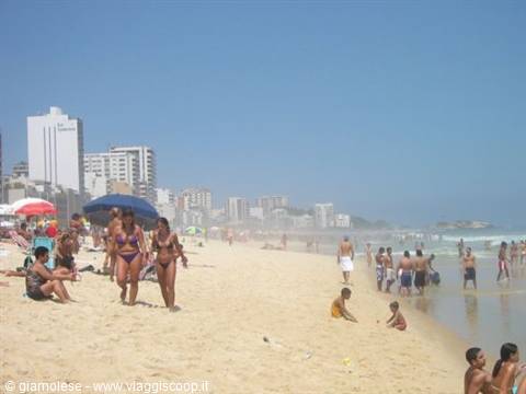 Beachgoers walk on Ipanema sand, high-rises and umbrellas, bright sun