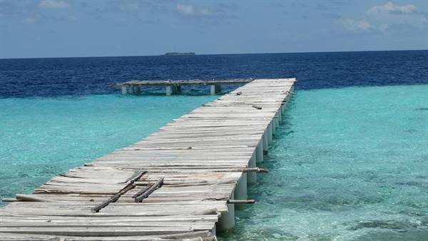 Weathered wooden jetty stretching over turquoise water toward deep blue sea