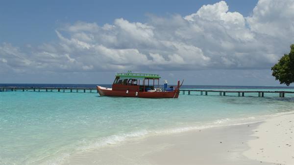 Red wooden boat moored at the pier over turquoise lagoon and white sand