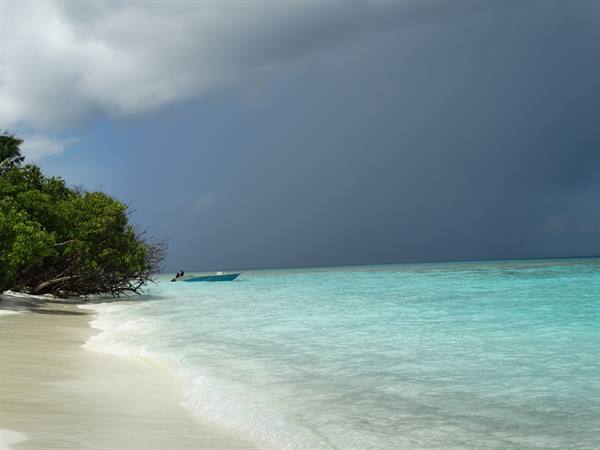 Blue motorboat on turquoise water, white sand beach, trees and dark clouds