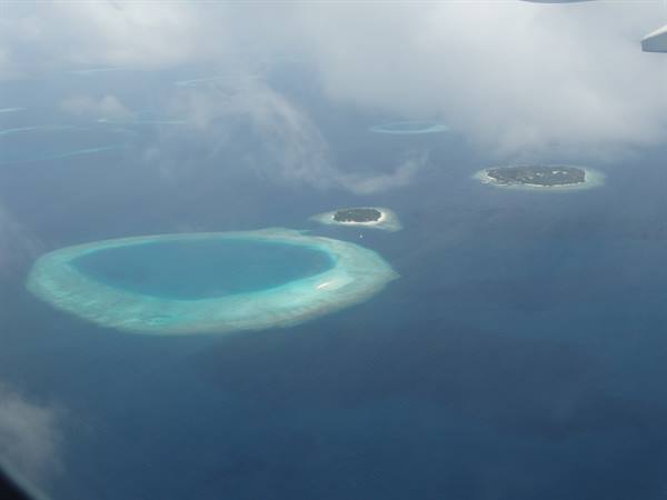 Turquoise coral atolls seen from the airplane through clouds over the ocean