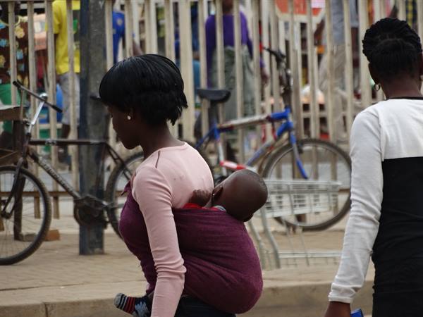 Woman carrying a baby wrapped in purple cloth walks past bicycles