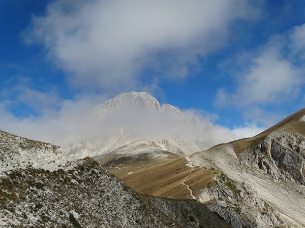 Hiker trail toward Corno Grande through clouds and limestone slopes