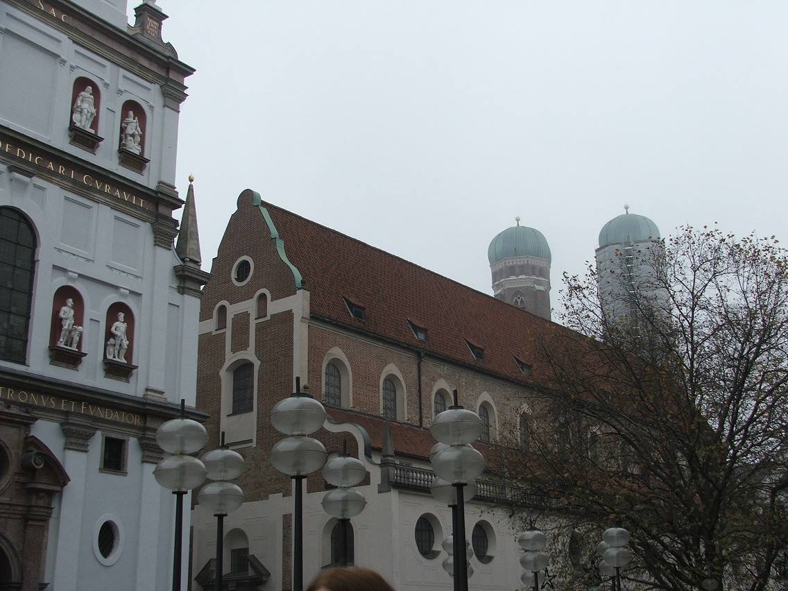 Facciata con statue e chiesa in mattoni con torri a cupola verde, München