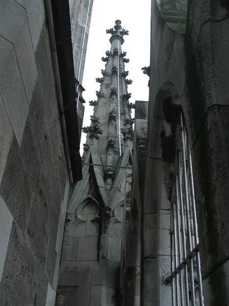 Gothic stone spire between marble walls of Milan Cathedral, grey sky