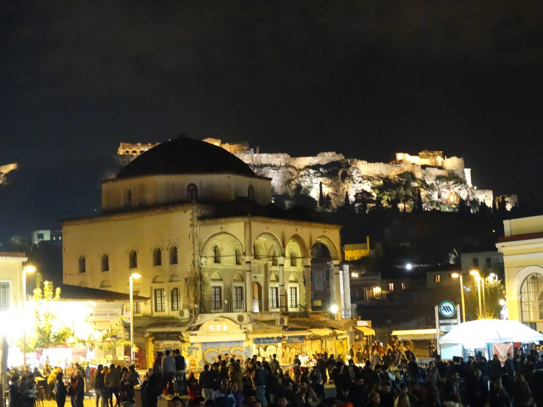 Piazza Monastiraki di notte con folla e l'Acropoli illuminata sullo sfondo