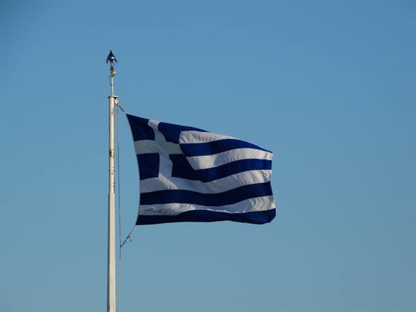 Greek flag waving from a tall white pole against blue sky