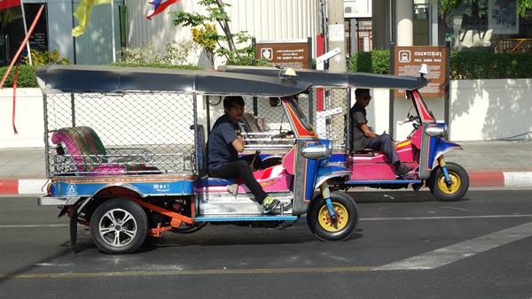 Two colorful tuk-tuks with drivers waiting on the street