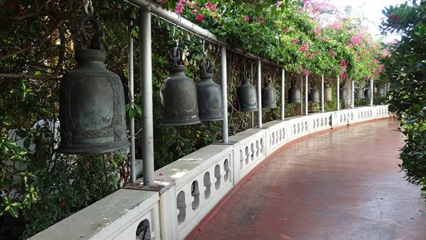 Bronze bells hanging along the Golden Mount railing in Bangkok, amid bougainvillea