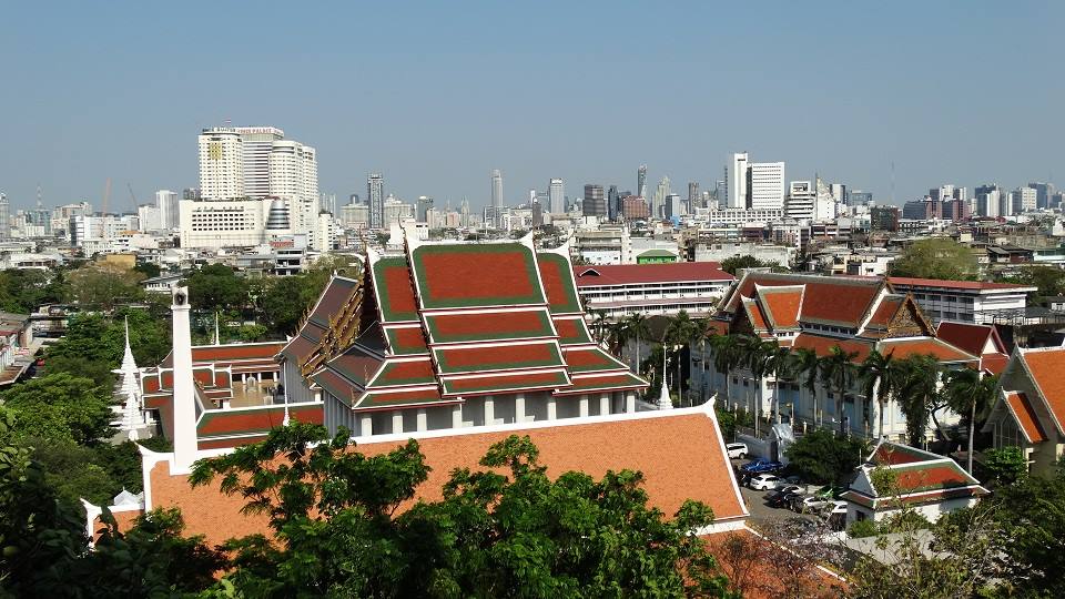 Tetti rossi e dorati di un tempio buddista, grattacieli di Bangkok sullo sfondo