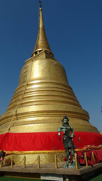 Golden stupa with red cloth band and bronze guardian statue under blue sky
