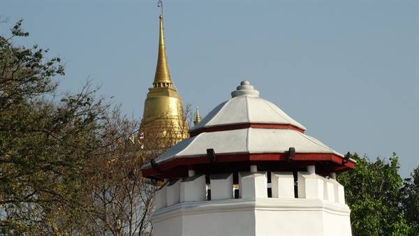 White pavilion with red roof in front of a golden stupa, blue sky