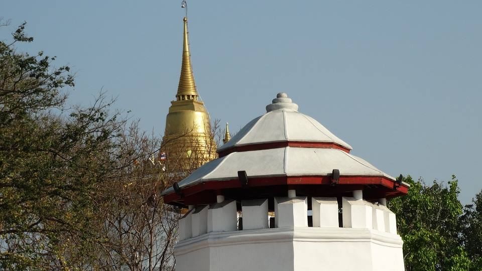 Padiglione bianco con tetto rosso davanti a uno stupa dorato, cielo azzurro