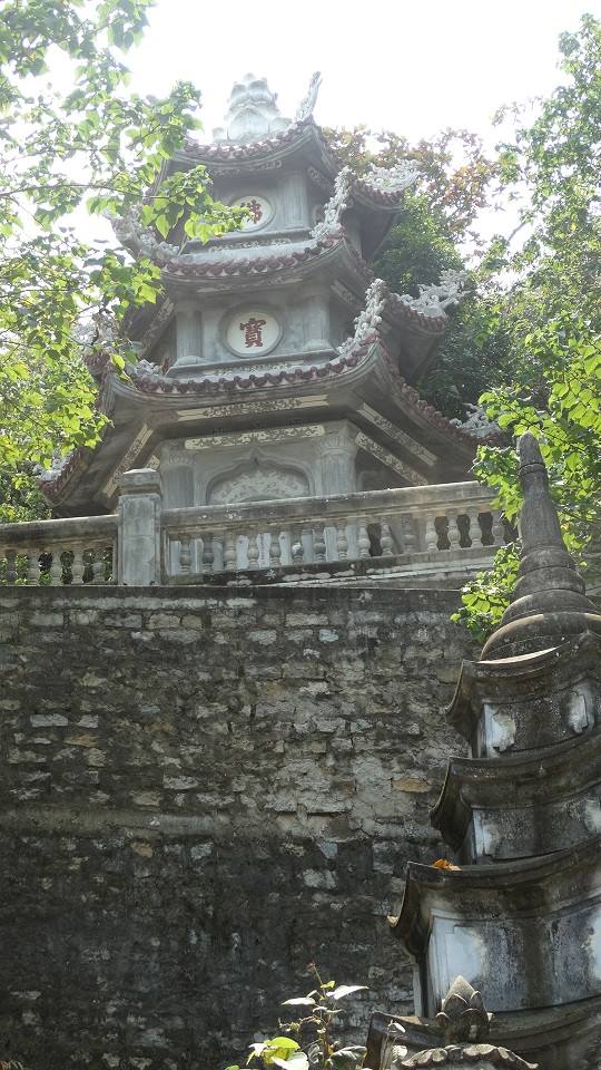 Pagoda buddhista in pietra tra alberi, muretto scolpito e torre funeraria