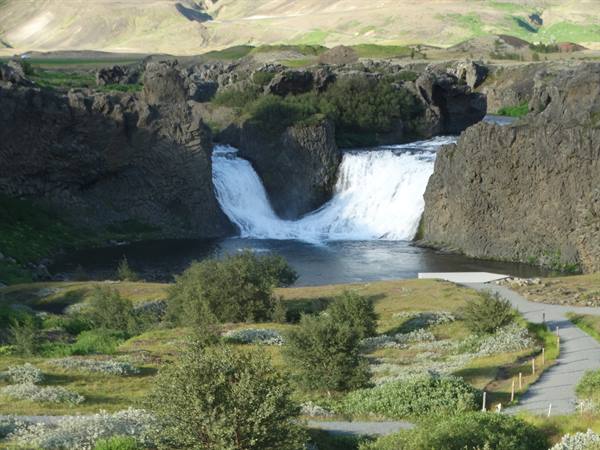 Twin waterfall between black volcanic rocks, gravel path and green bushes, daylight