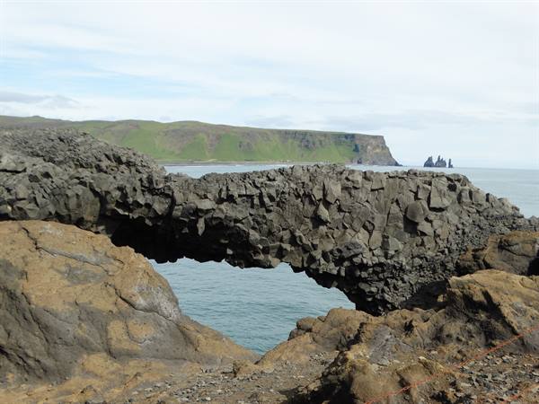 Basalt rock arch over the sea at Dyrhólaey, green cliffs and sea stacks behind