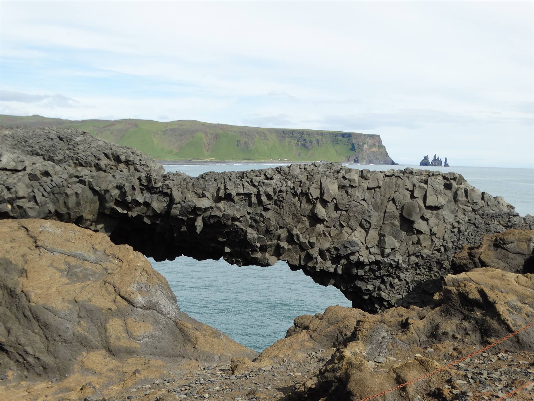 Arco di roccia basaltica sul mare a Dyrhólaey, scogliere verdi e faraglioni sullo sfondo