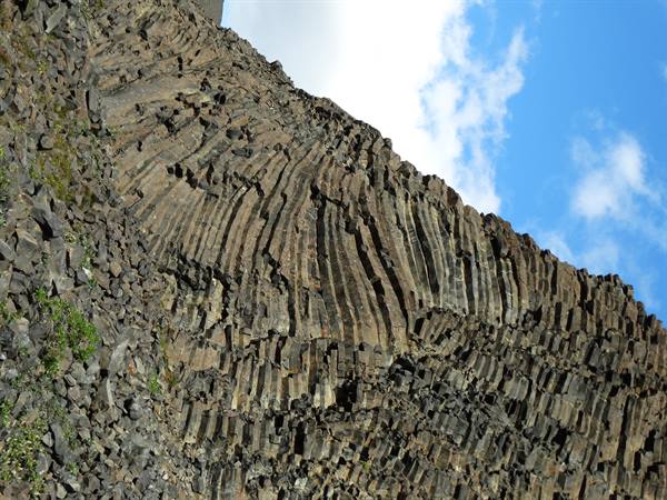 Curved basalt columns against a blue sky with white clouds