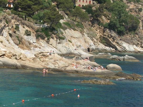 Swimmers on granite rocks, turquoise water, houses and pines on the cliff