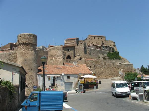 Stone village with medieval tower and hilltop houses, vans parked below