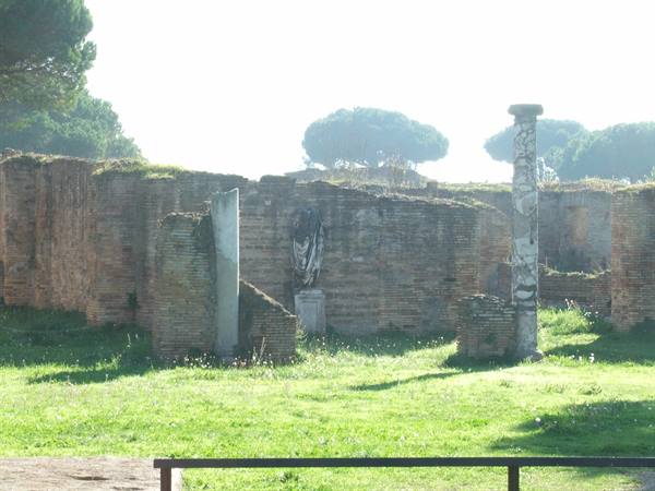 Brick ruins with columns and a statue among the grass, Ostia Antica