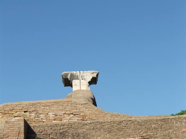 Ancient marble fragment atop Roman brick walls against a blue sky