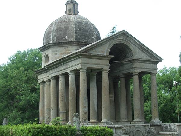 Stone temple with Doric columns and dome, surrounded by green trees
