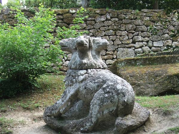 Stone statue of the three-headed dog Cerberus sitting before a mossy wall