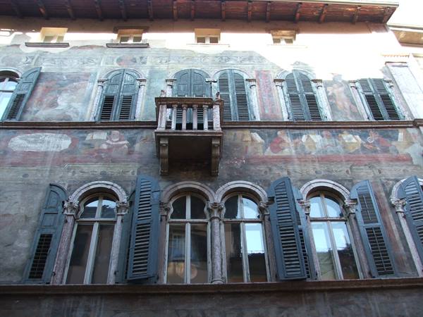 Frescoed facade with wooden balcony and green shutters on arched windows